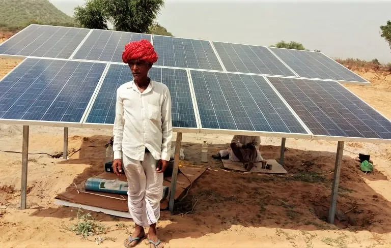 राजस्थान के एक गांव में एक ग्रामीण अपने सौर पैनल के पास जिससे उनका सौर पम्प चलता है। तस्वीर- अग्रीविजय