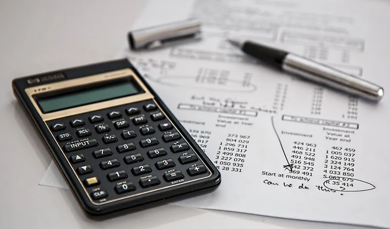 A black calculator near a ballpoint pen on white printed paper